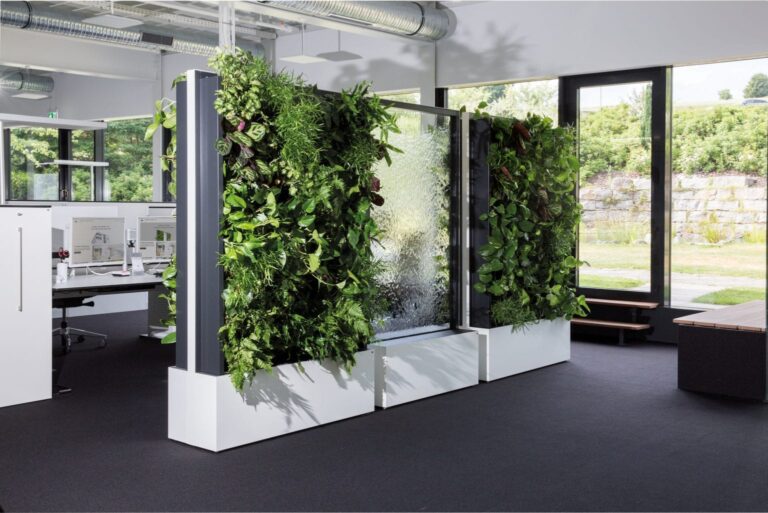 Büro mit Pflanzenwand, Schreibtischen und Blick auf grüne Landschaft.