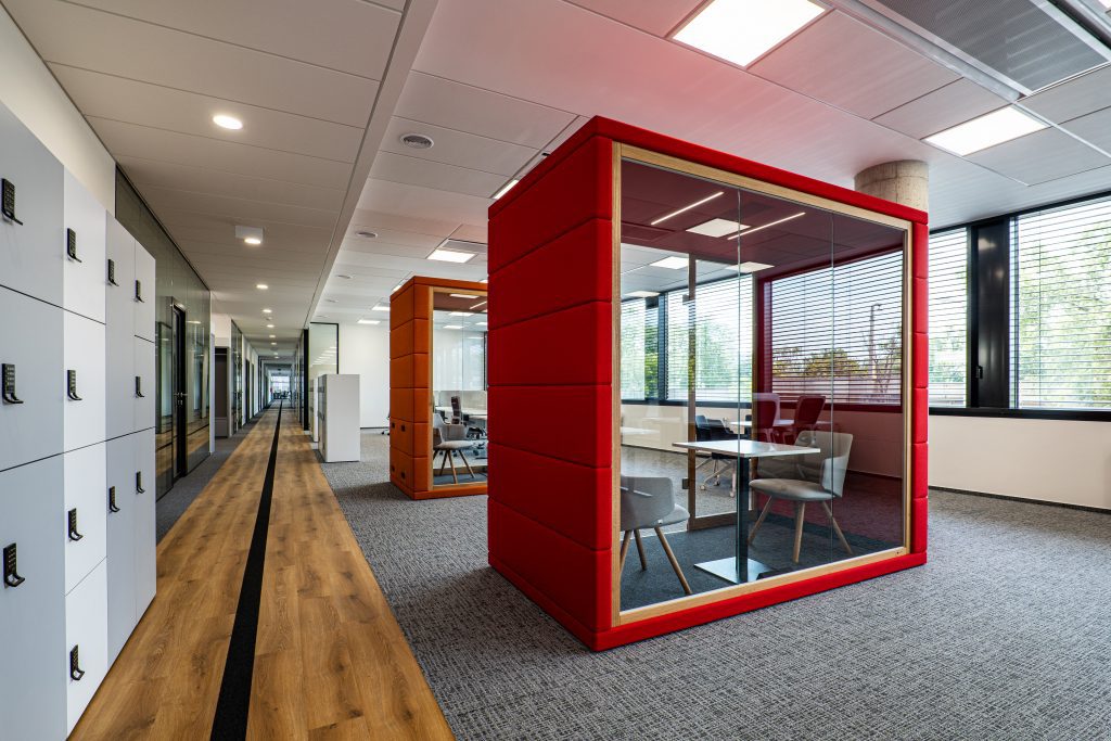 Moderner Büroflur mit gläsernen Besprechungsräumen und Holzböden.