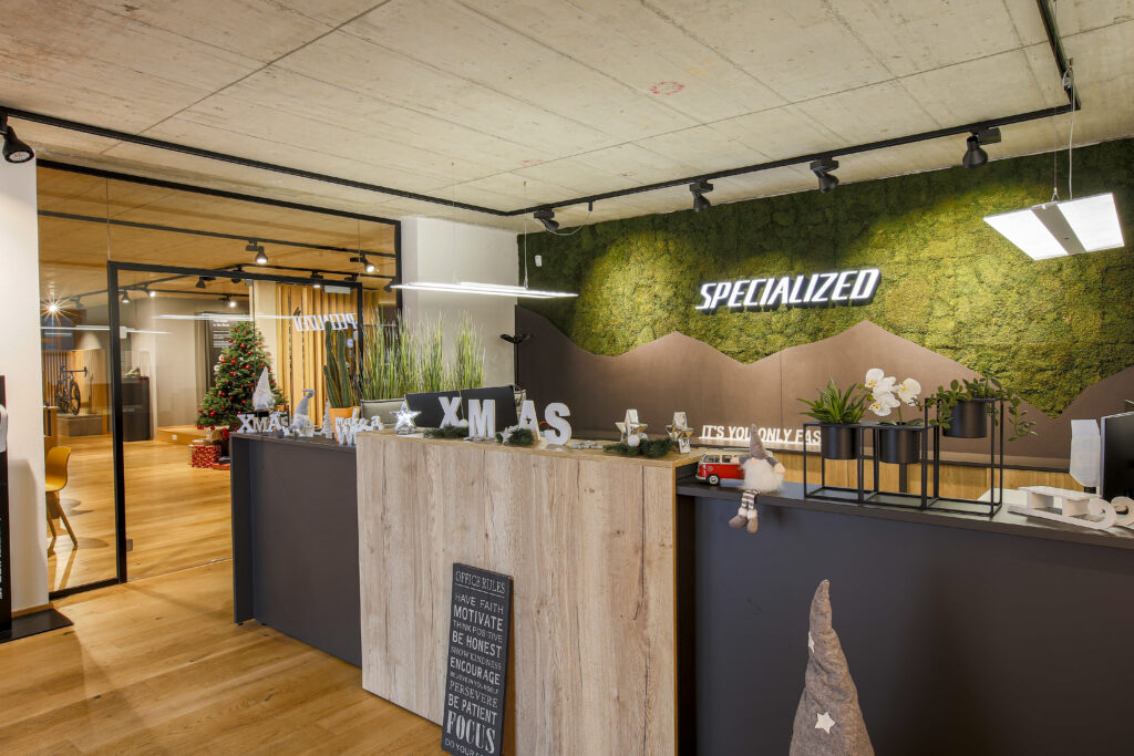 Empfangstheke vor Mooswand mit „SPECIALIZED“-Logo und weihnachtlicher Dekoration. ChatGPT fragen