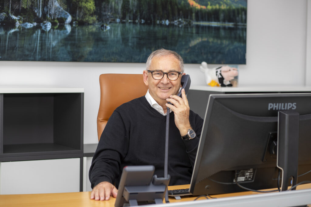 Berater Peter Lech telefoniert lächelnd am Schreibtisch mit Computer im Büro.