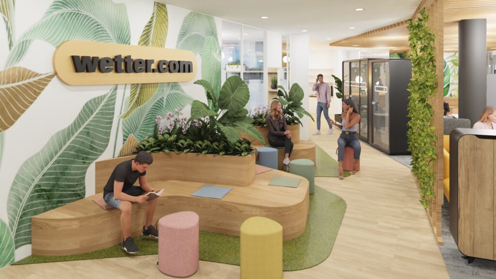 Menschen sitzen auf Holzbank im begrünten Wartebereich mit bunten Hockern.