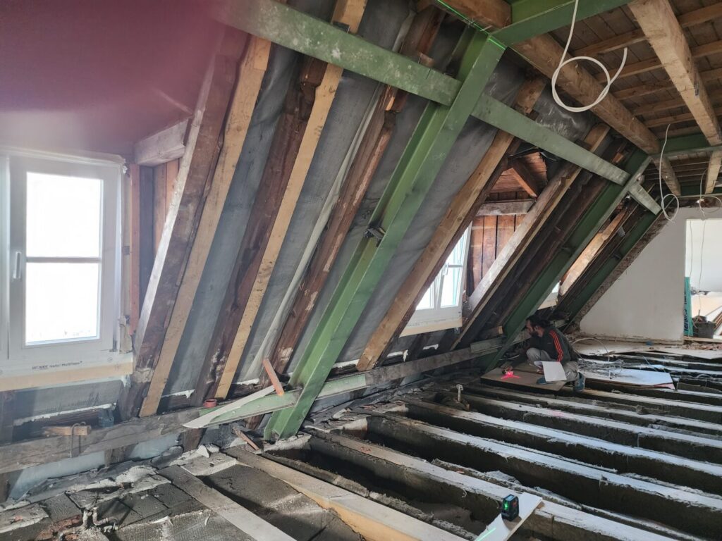 Dachstuhl mit offenen Balken und freigelegtem Boden in Renovierungs- oder Rohbauzustand.