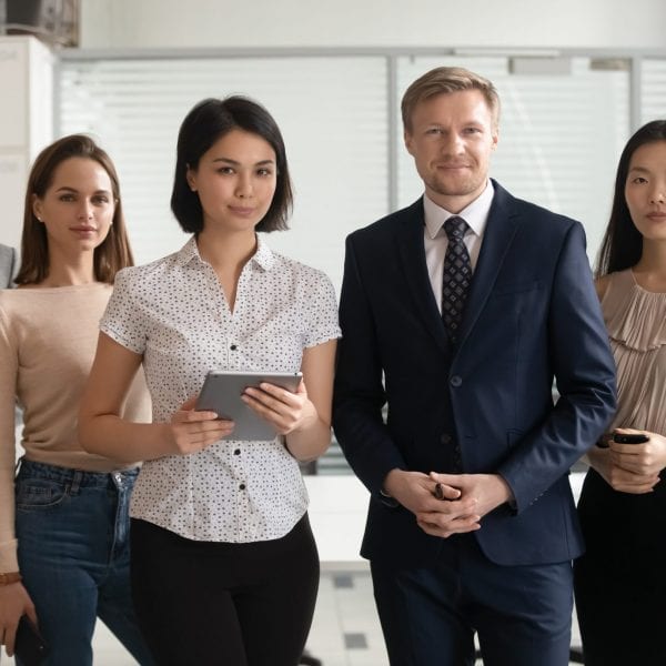 Portrait of successful diverse employees team standing in office Portrait of happy smiling diverse employees team standing in office, holding phone and tablet, posing for company photo together, looking at camera, workers group motivated for business success