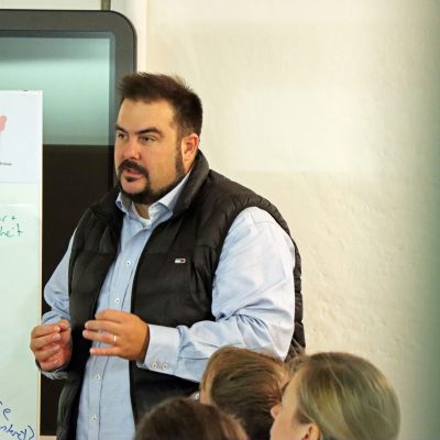 Mann erklärt Inhalte an Whiteboard bei interaktivem Workshop im kleinen Kreis.