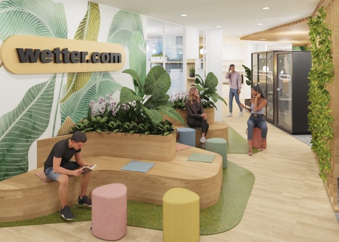 Menschen sitzen auf Holzbank im begrünten Wartebereich mit bunten Hockern.
