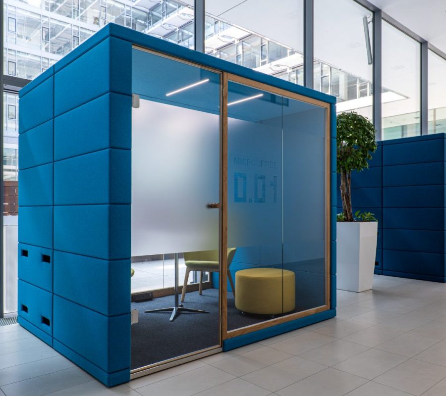 Blaue Bürokabine „MICROOFFICE 0.01“ mit Stuhl und Ottomane in modernem Büro.