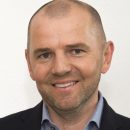 Porträt eines Mannes im Anzug, lächelnd, mit hellem Hintergrund