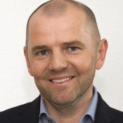 Porträt eines Mannes im Anzug, lächelnd, mit hellem Hintergrund